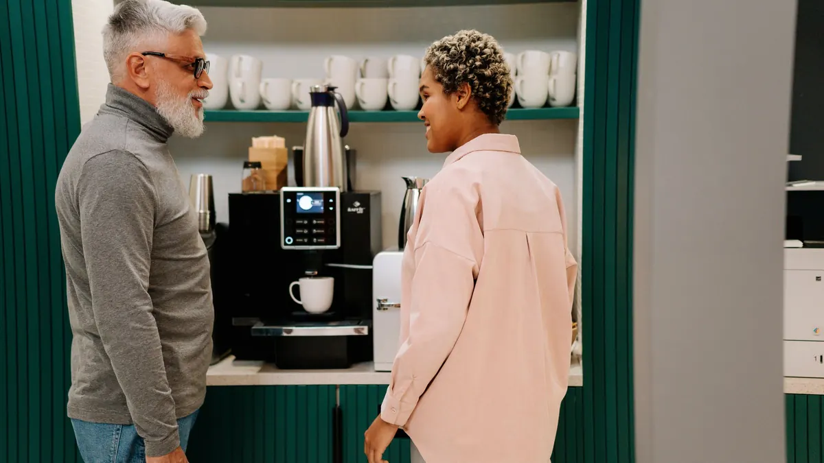 Dos personas conversando junto a la máquina de café de una oficina